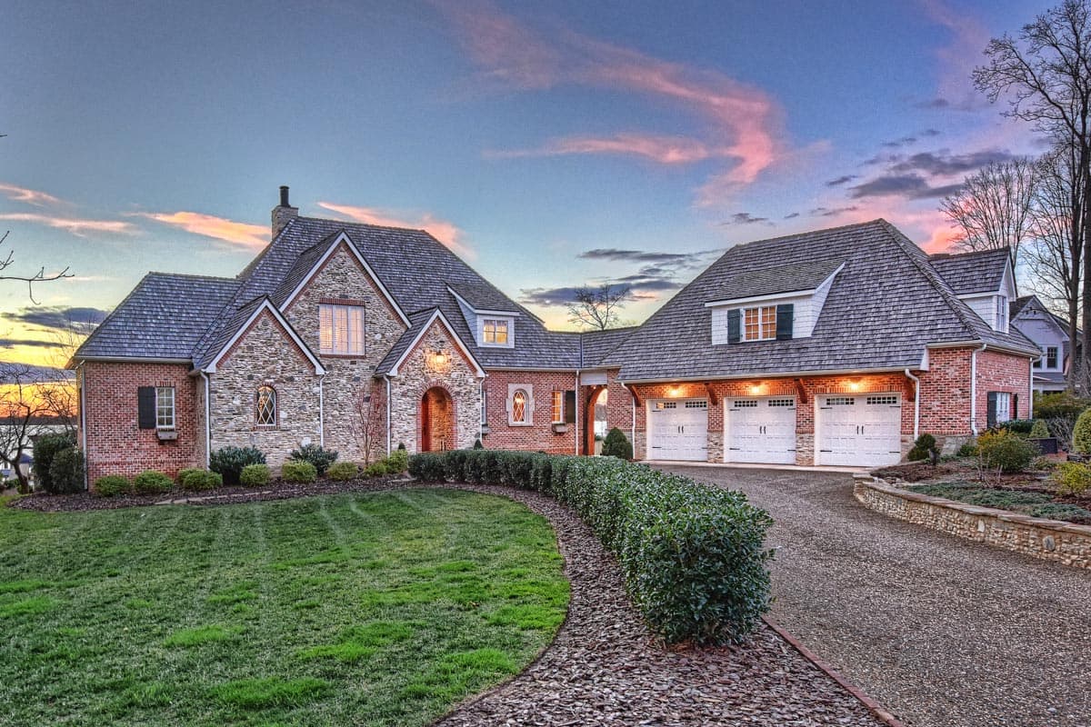 House plan exterior with stone and brick facade, arched entry, multiple gables, and a three-car garage.