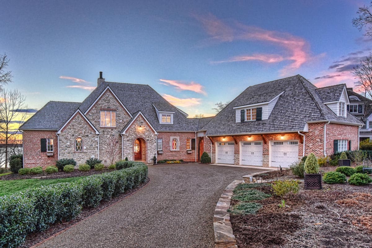 House plan exterior with brick and stone facade, steeply pitched rooflines, dormers, and a three-car garage.