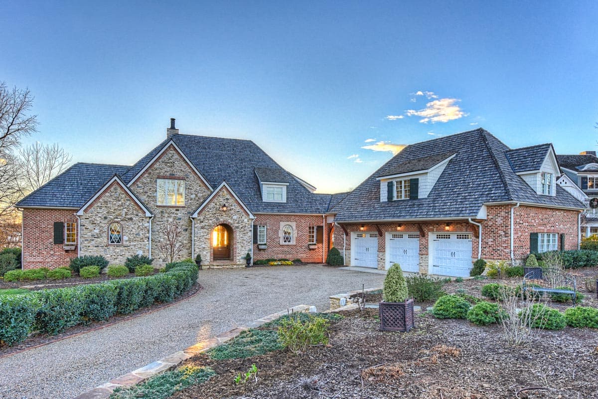 House plan exterior featuring a two-story design with a stone and brick facade, multiple gables, and attached garage with dormers.