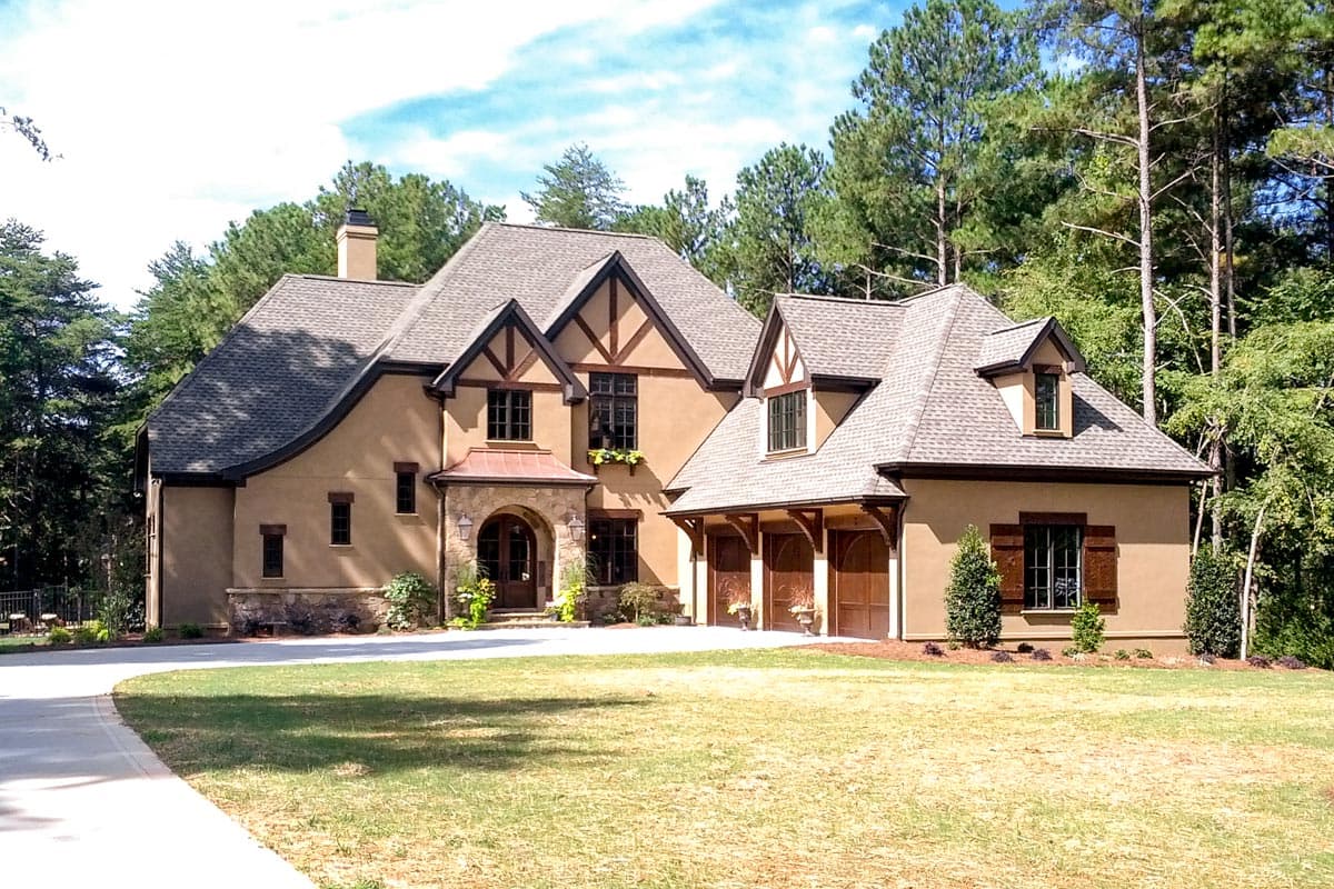 House plan exterior in Tudor style with multiple gables, dormers, arched entry, and attached garage. Two stories.