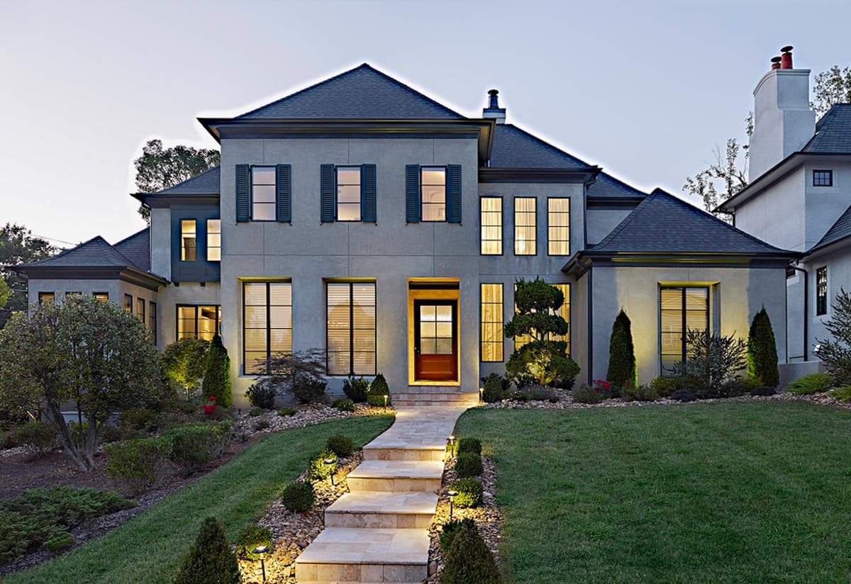 House plan exterior. Two-story with gabled roof, shutters, and a stone walkway. Features include multiple dormers and a symmetrical facade.