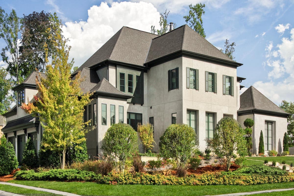 House plan exterior: two-story stucco home with multiple gables, dark trim, shutters, and varied window arrangements.