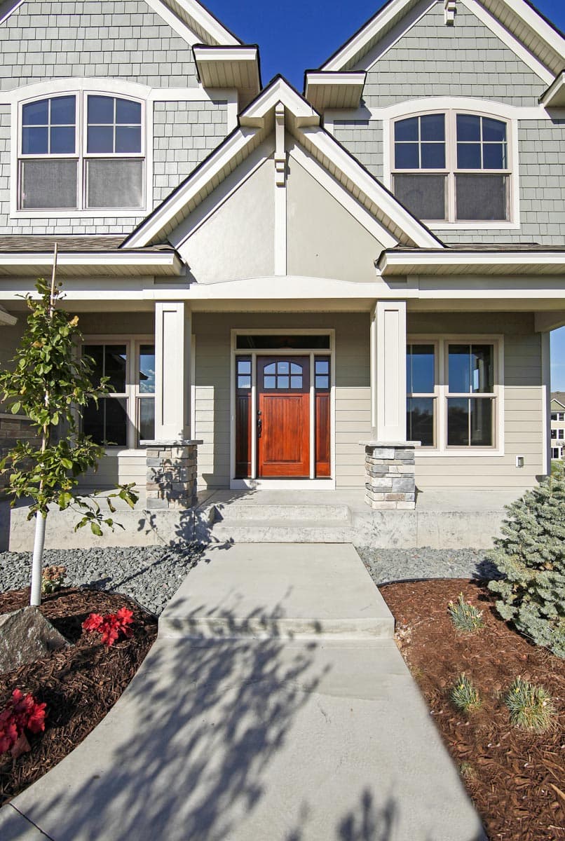 House plan exterior featuring a covered porch with stone-clad columns, a multi-pane front door, and gable dormers.