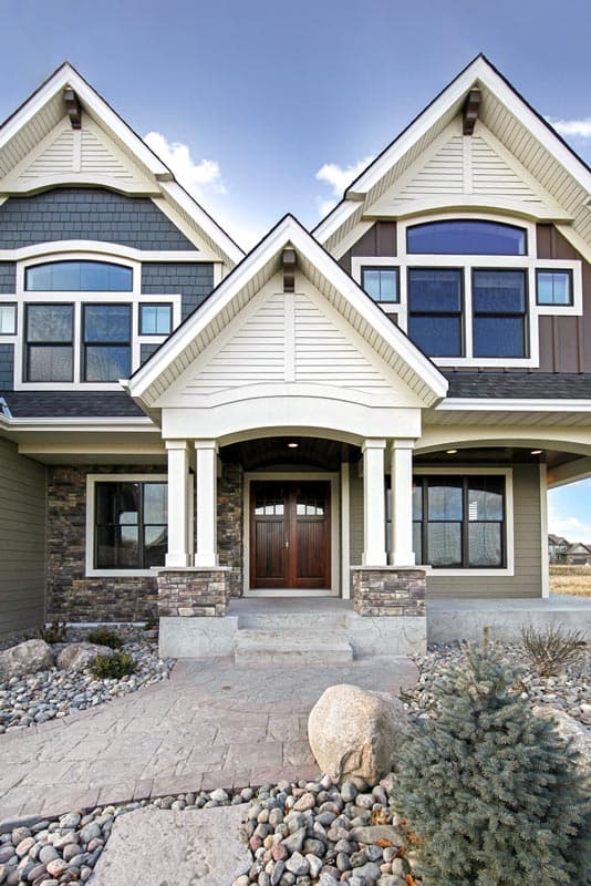 House plan exterior: Two-story modern house with prominent gables, arched dormers, stone accents, and a covered entry with double wood doors.