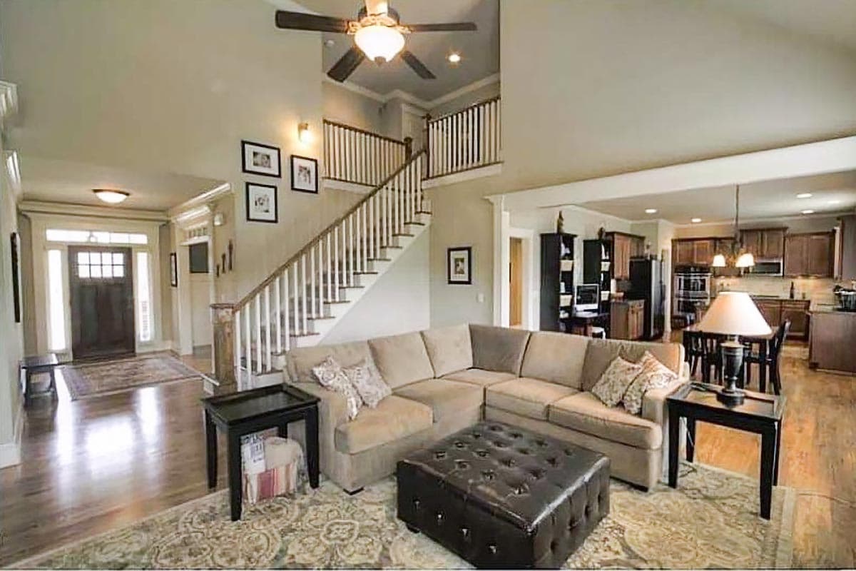 Interior view of a living room with a sectional sofa, fireplace, and adjacent kitchen. Open layout with a staircase and entry foyer.