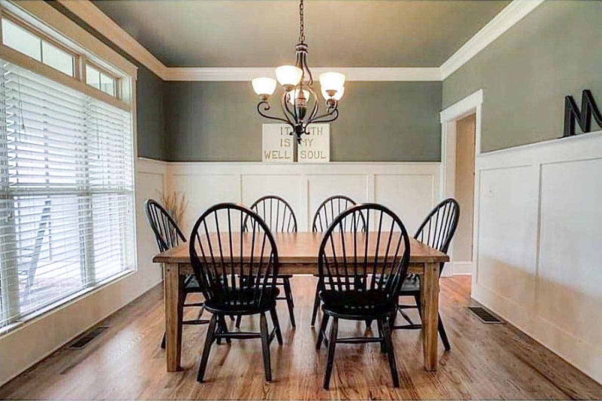 Dining room with wooden table, black Windsor chairs, wainscoting, and a large window.