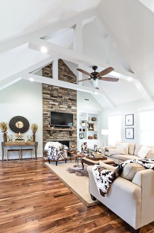 Interior view of a living room with a stone fireplace, vaulted ceiling with exposed beams, and wood floors.