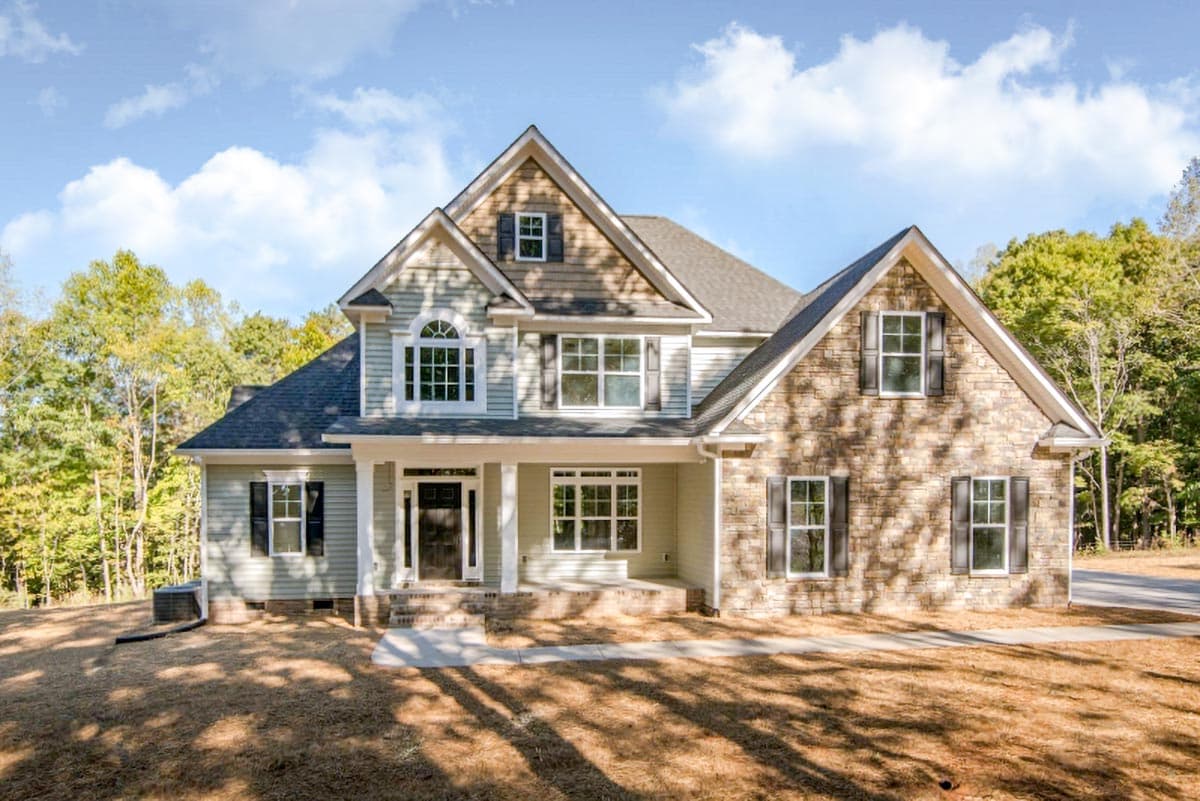 House plan exterior. Two-story with gabled roof, front porch, and dormer windows. Stone and siding exterior with multiple windows.