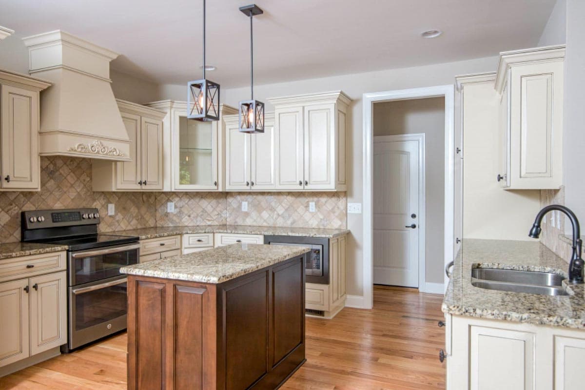 Kitchen interior with cream cabinets, granite countertops, decorative range hood, island, and hardwood floors.