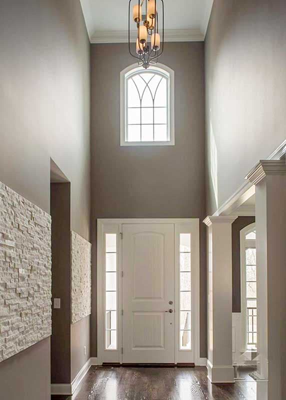 Two-story foyer with a white front door, sidelights, arched window above, and decorative stone wall accents.
