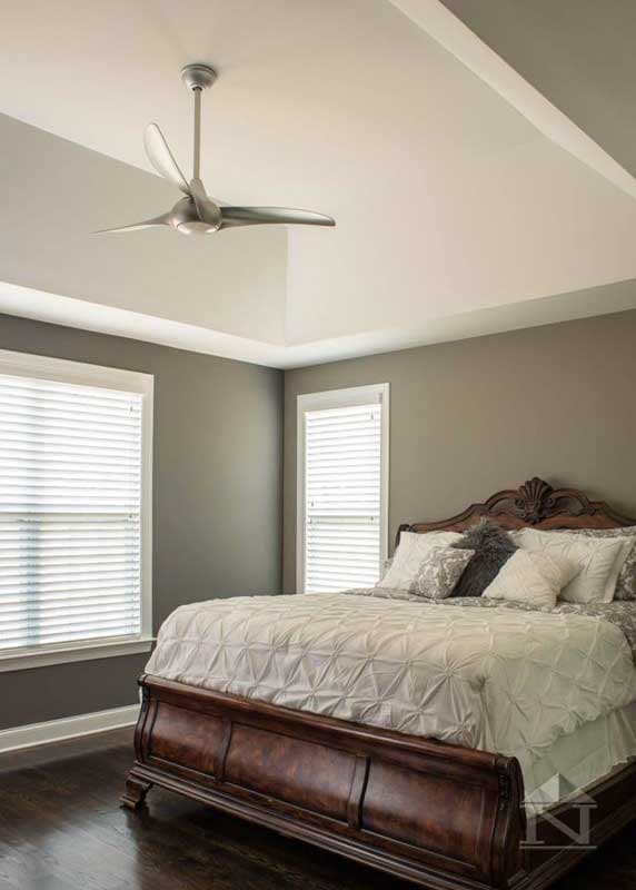 Bedroom interior with tray ceiling, modern ceiling fan, two windows, and a dark wood bed frame.