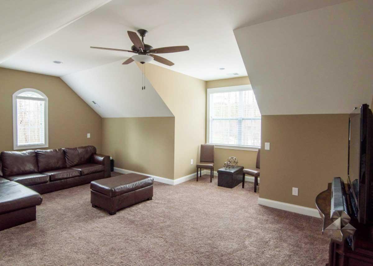 Interior view of a living space with vaulted ceilings, a brown sectional sofa, ottoman, and two windows.