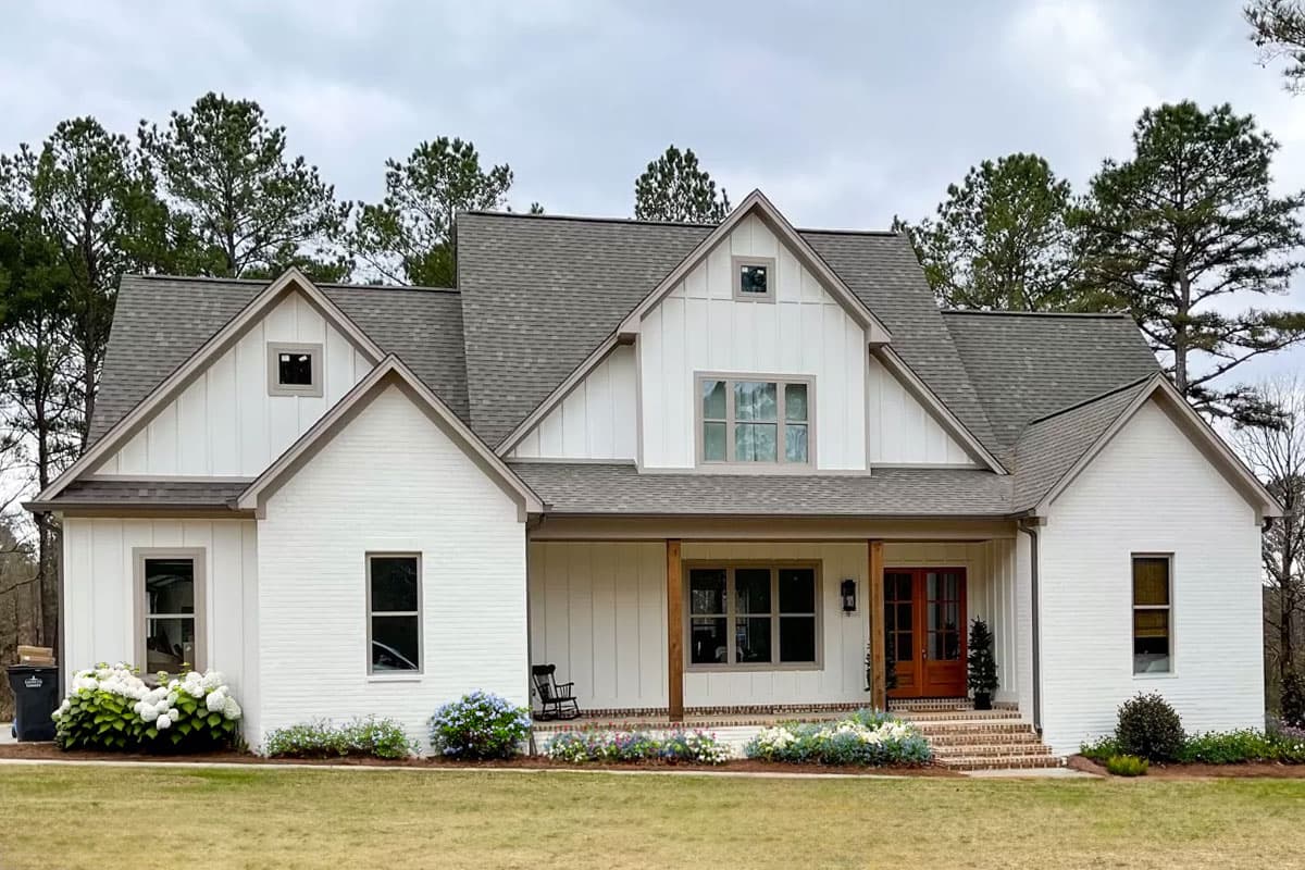 House plan exterior. Two-story Modern Farmhouse with gables, a covered porch with wooden supports, and brick facade.