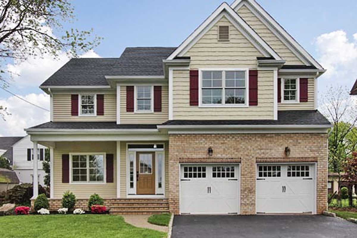 Two-story house plan exterior with beige siding, red shutters, covered front porch, and attached two-car garage with brick facade.