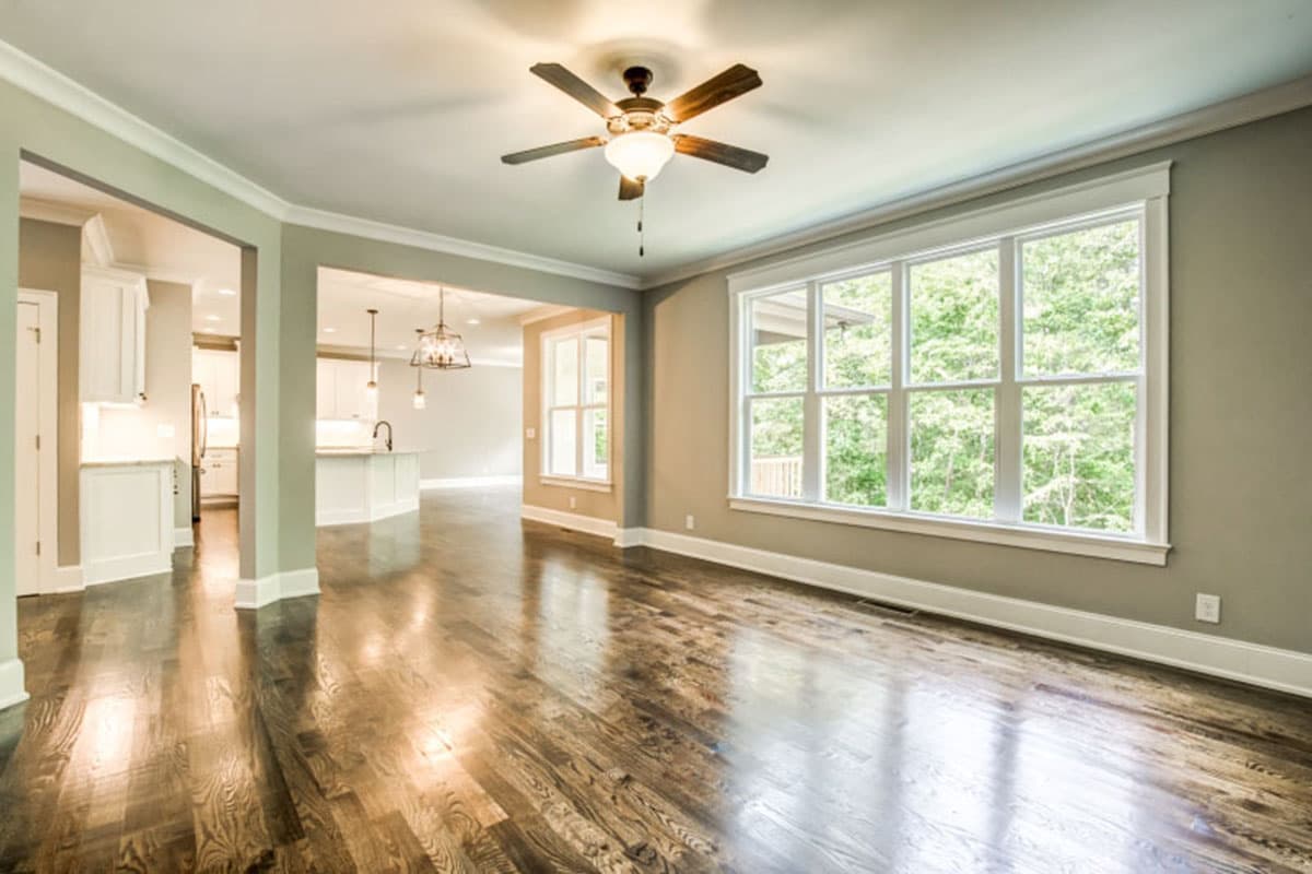 Open concept living area with a kitchen island, dark hardwood floors, and large windows overlooking trees.