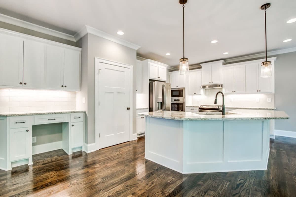 Interior view of a kitchen with a large island, white cabinets, granite countertops, and a built-in desk.