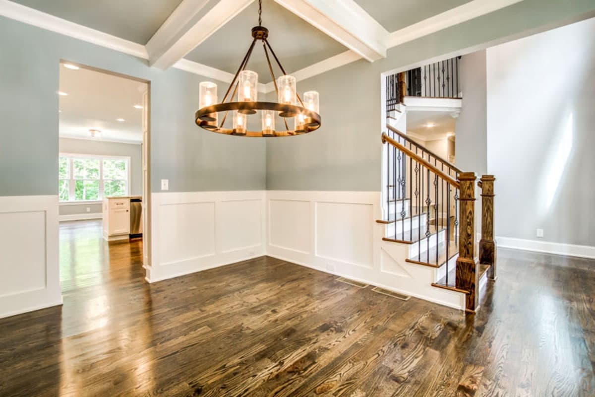 Interior view of a dining area with a coffered ceiling, wrought iron chandelier, wainscoting, and staircase.