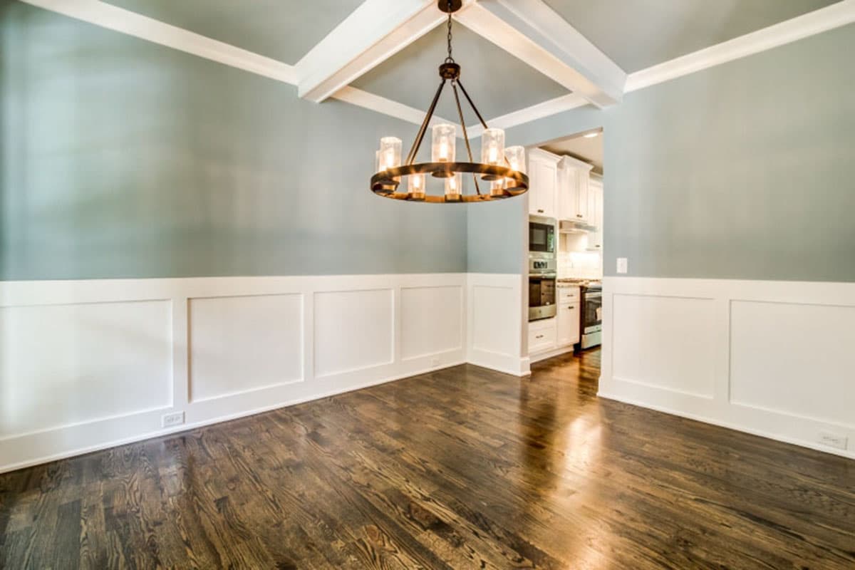 Dining room with coffered ceiling, wainscoting, hardwood floors, and view into kitchen.