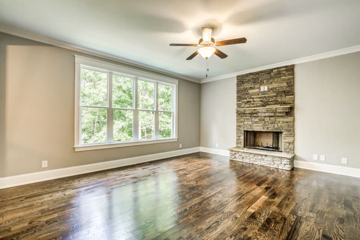 Interior view of room with large window, stone fireplace, hardwood floors, and ceiling fan.