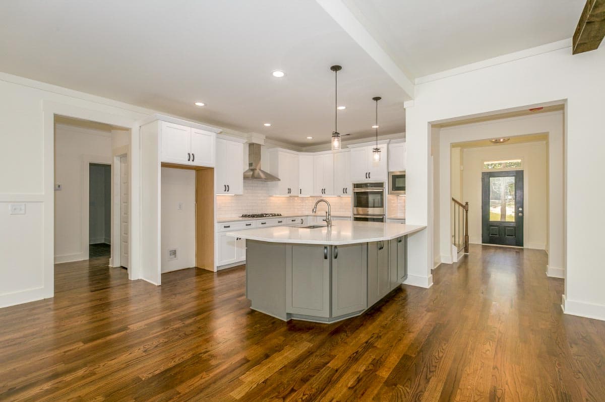 Interior view of a white kitchen with a large gray island, stainless steel appliances, subway tile backsplash, and an open view to the entryway.