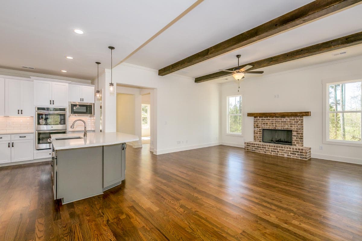 Open-concept living area with kitchen island, brick fireplace, and exposed ceiling beams.