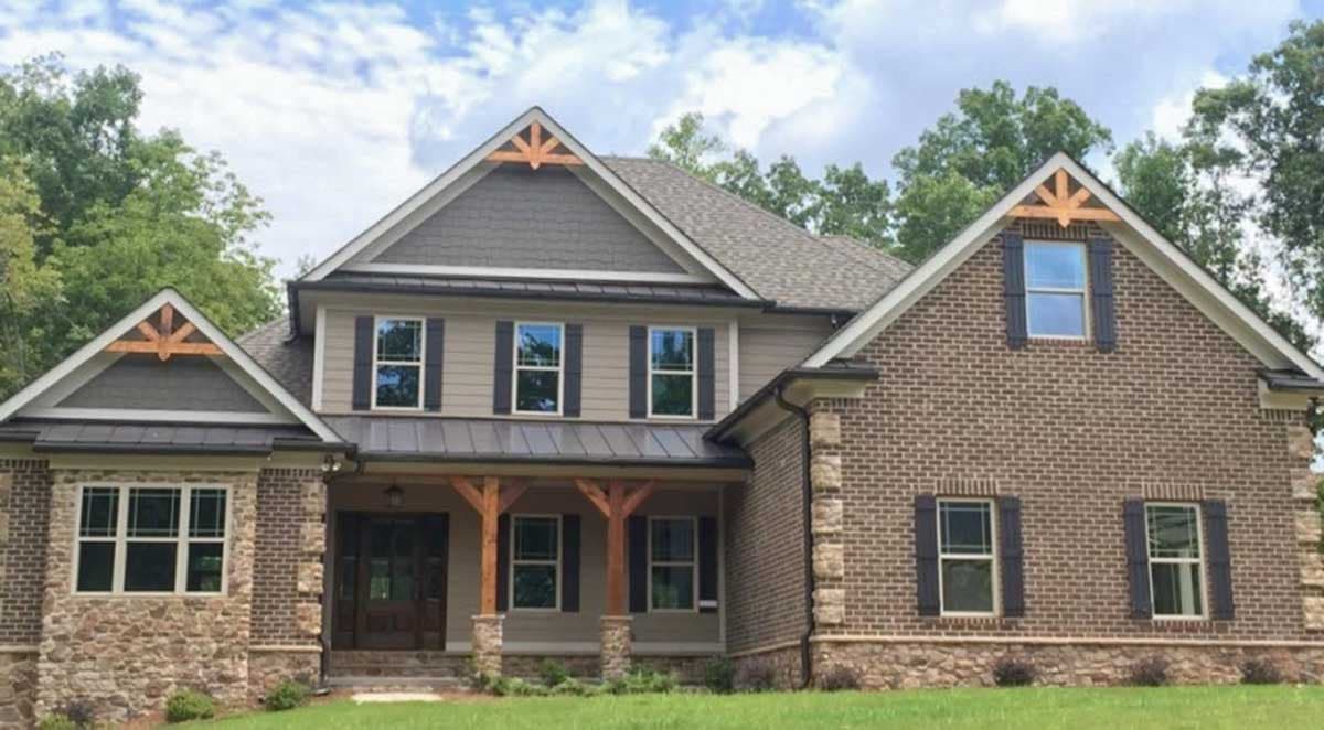 House plan exterior: Two-story home with stone and brick facade, metal roof, and covered porch with wooden beams and decorative gables.