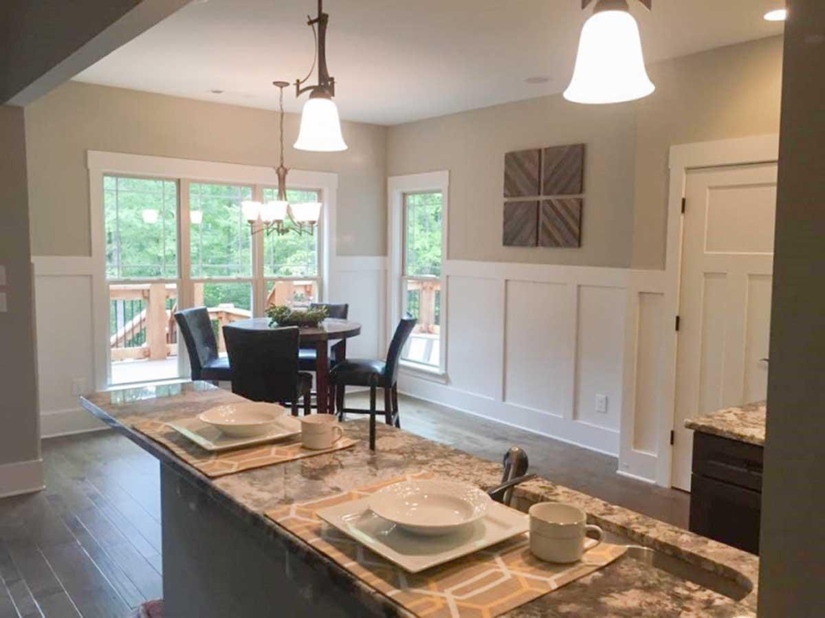 Interior view of dining area with table, chairs, large windows, and kitchen counter. Board and batten wainscoting on walls.