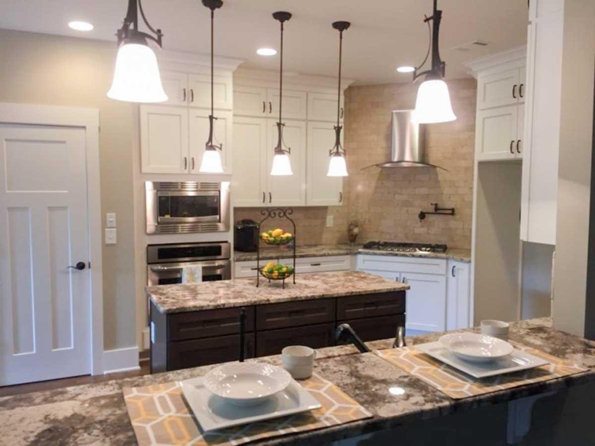 Kitchen featuring a central island with dark cabinetry, granite countertops, white upper cabinets, stainless steel appliances, and pendant lighting.