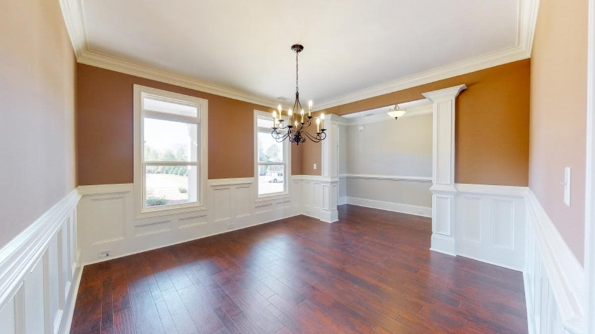 Dining room with dark hardwood floors, white wainscoting, two windows, and a chandelier.