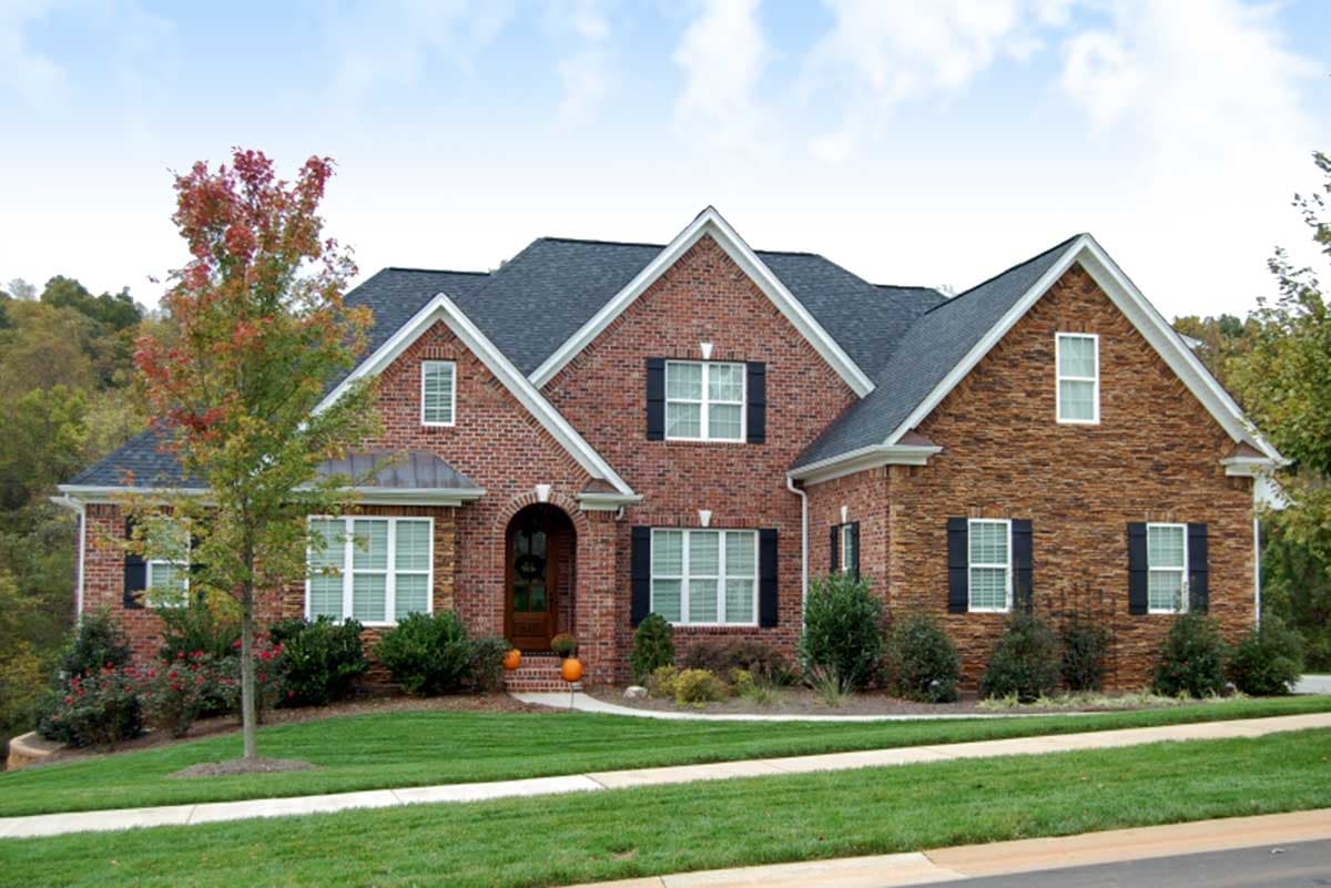 House plan exterior with brick and stone facade, gabled dormers, arched entryway, and multiple rooflines.