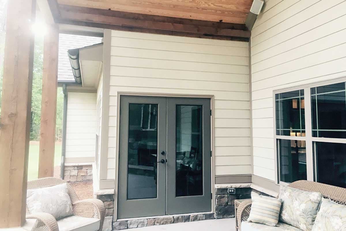 Exterior view of a house with a covered porch, double doors, and a large window. Features horizontal siding and stone accents.