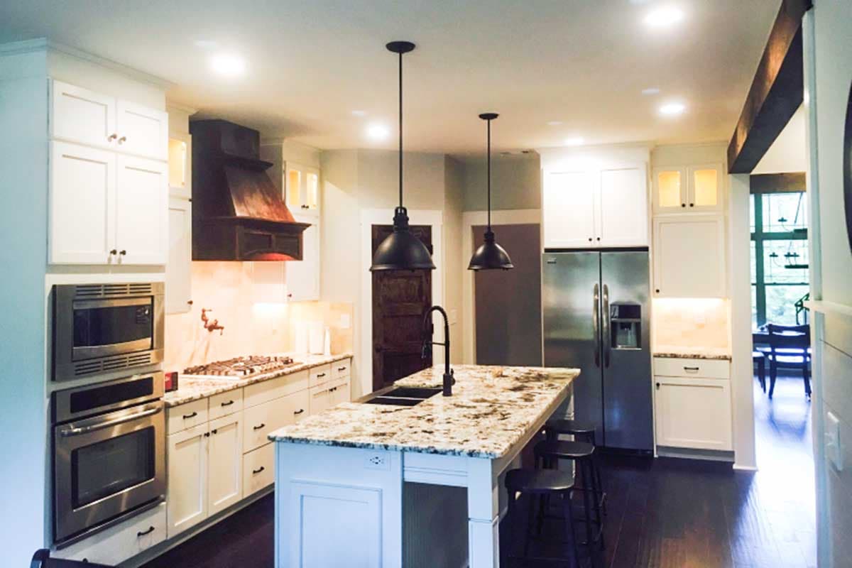 Kitchen with white cabinets, island with sink and seating, stainless steel appliances, and decorative range hood.