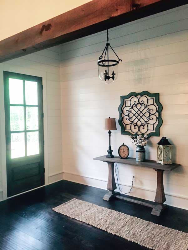 Interior view of a room with shiplap walls, dark wood floor, a dark paneled door, and a rustic console table.