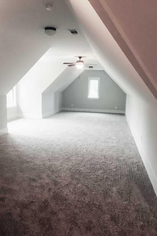 Attic space with sloped ceilings, carpet flooring, ceiling fan, and a single window.