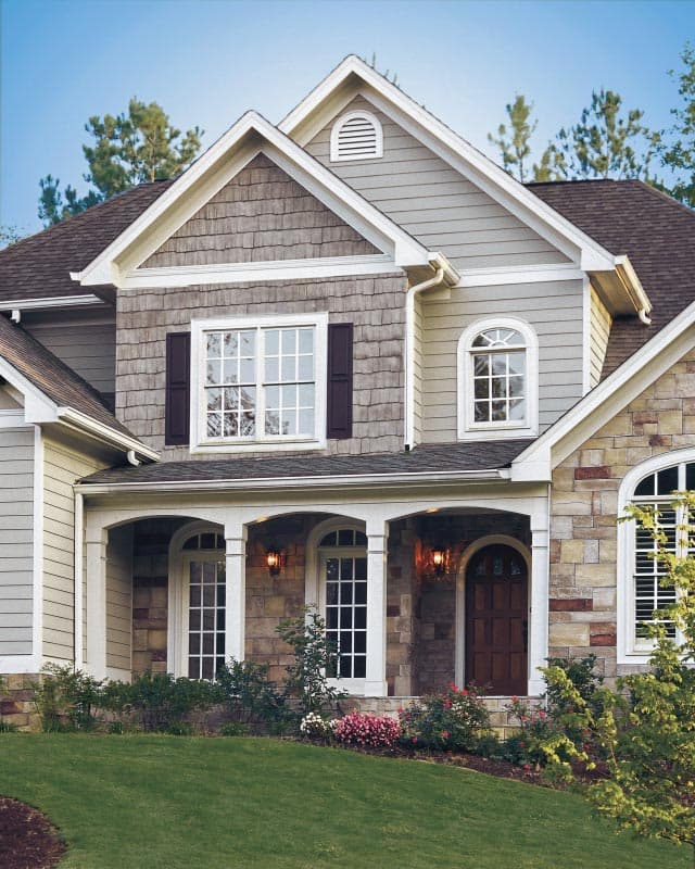 House plan exterior: Two-story home with stone and shingle siding, arched entry porch with square columns, gabled dormer, and multi-pane windows.