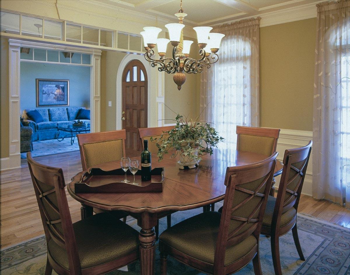 Dining room with oval table, chairs, chandelier, and an arched doorway leading to a living room.