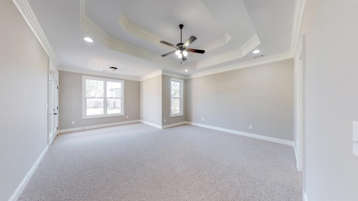 Interior view of a spacious room with a tray ceiling, ceiling fan, and multiple windows.