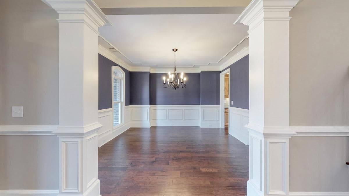 Formal dining room with wainscoting, chandelier, and hardwood floors, viewed between decorative columns.