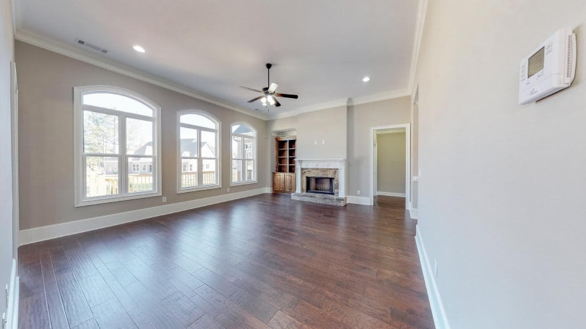 Living room with fireplace, built-in cabinetry, ceiling fan, and large arched windows with views of houses.