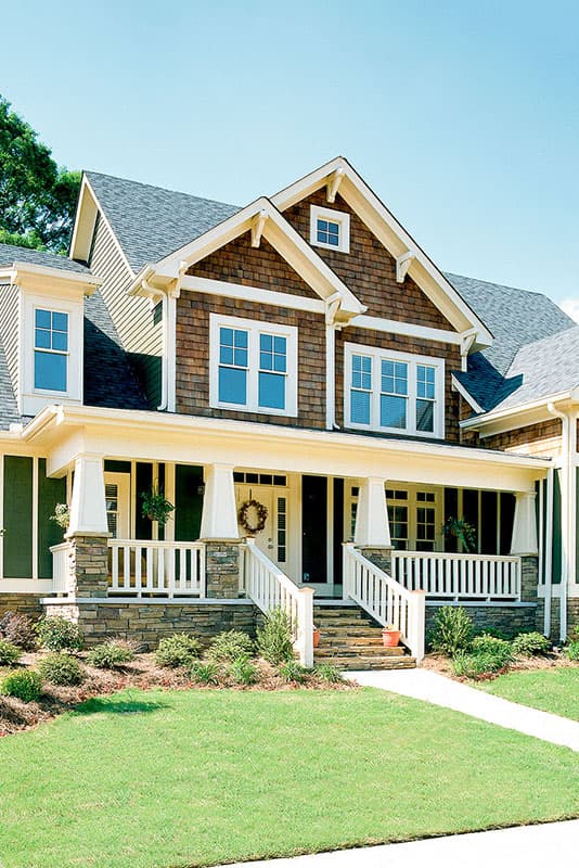 Craftsman house plan exterior with a wraparound porch, stone accents, multiple gables, and dormer windows.