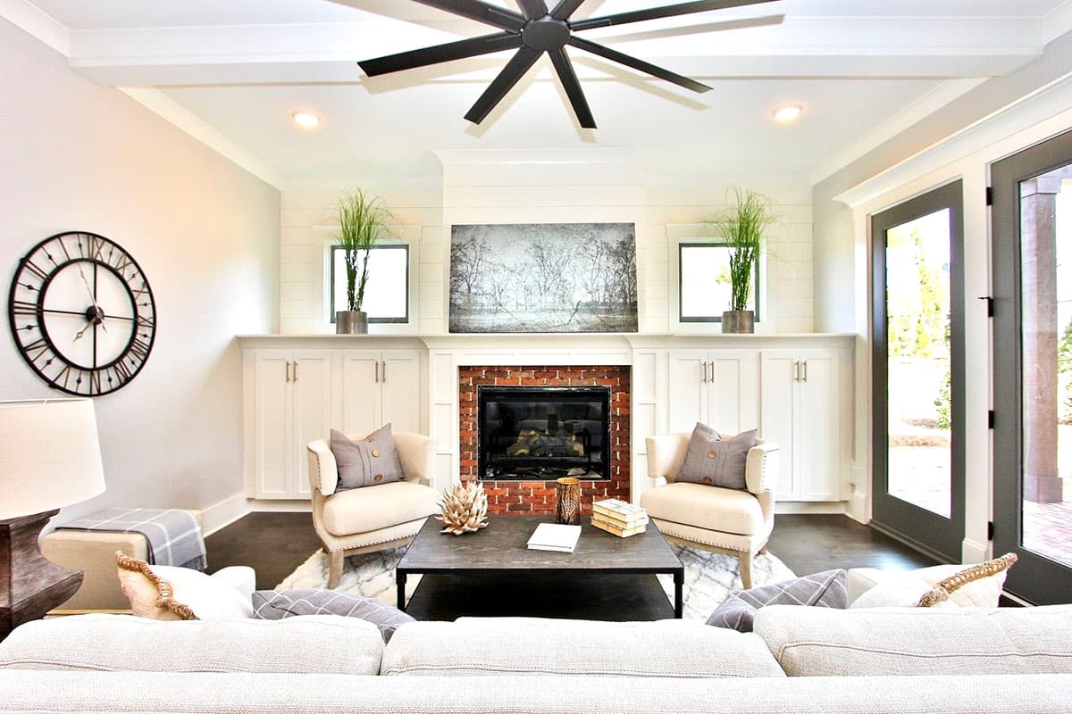 Living room with fireplace, built-in cabinets, coffered ceiling with fan, and glass doors.
