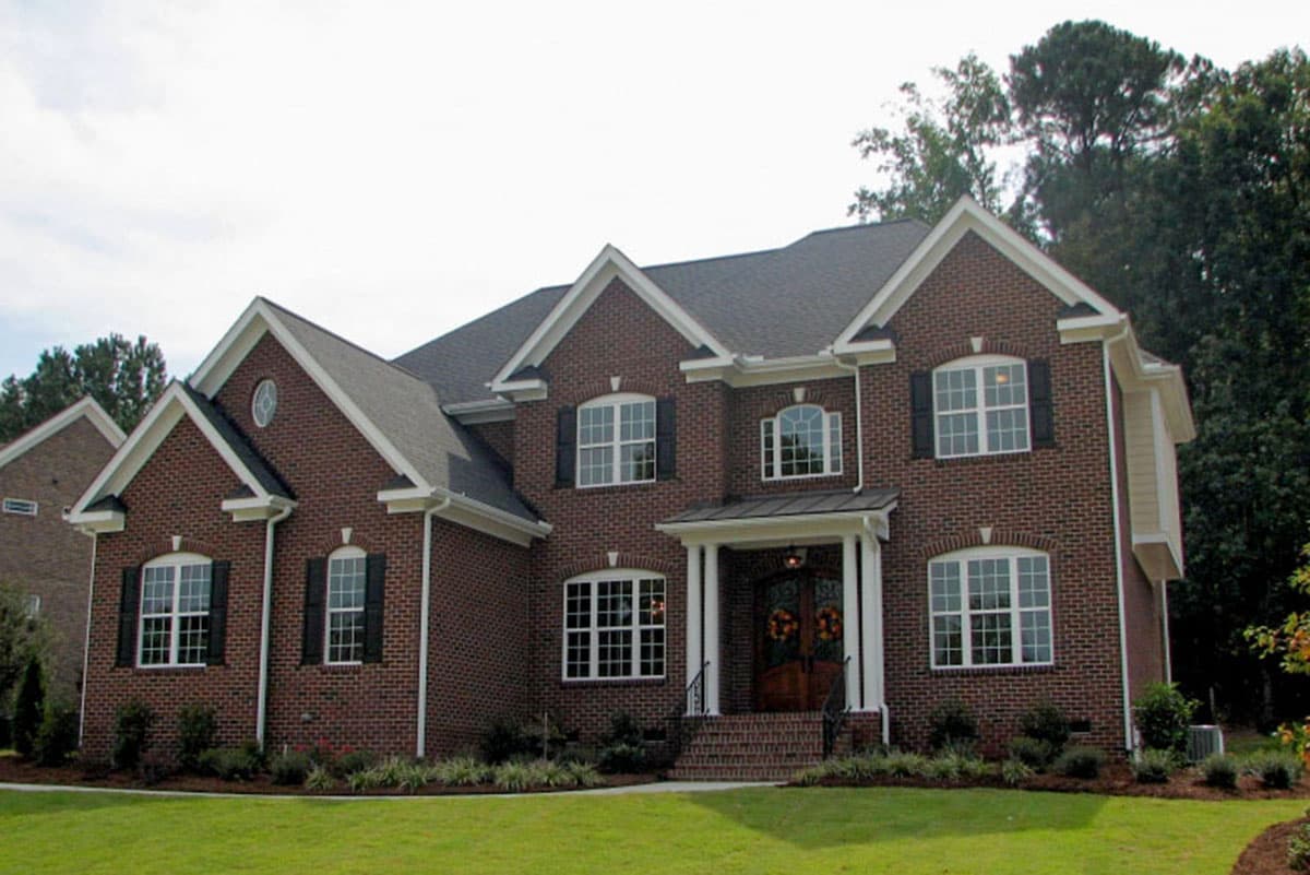 House plan exterior of a two-story brick home with arched windows, gables, dormers, and a covered front porch.