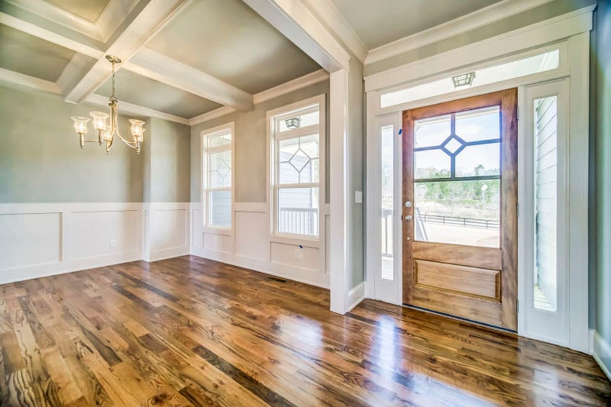 Interior view of a room with coffered ceiling, wainscoting, chandelier, and a wooden front door with glass inserts.
