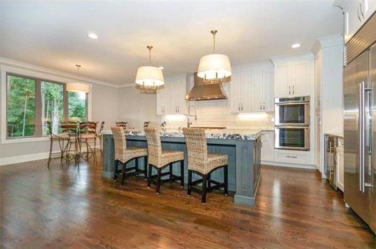 Kitchen featuring island with seating, stainless steel appliances, range hood, and large window.