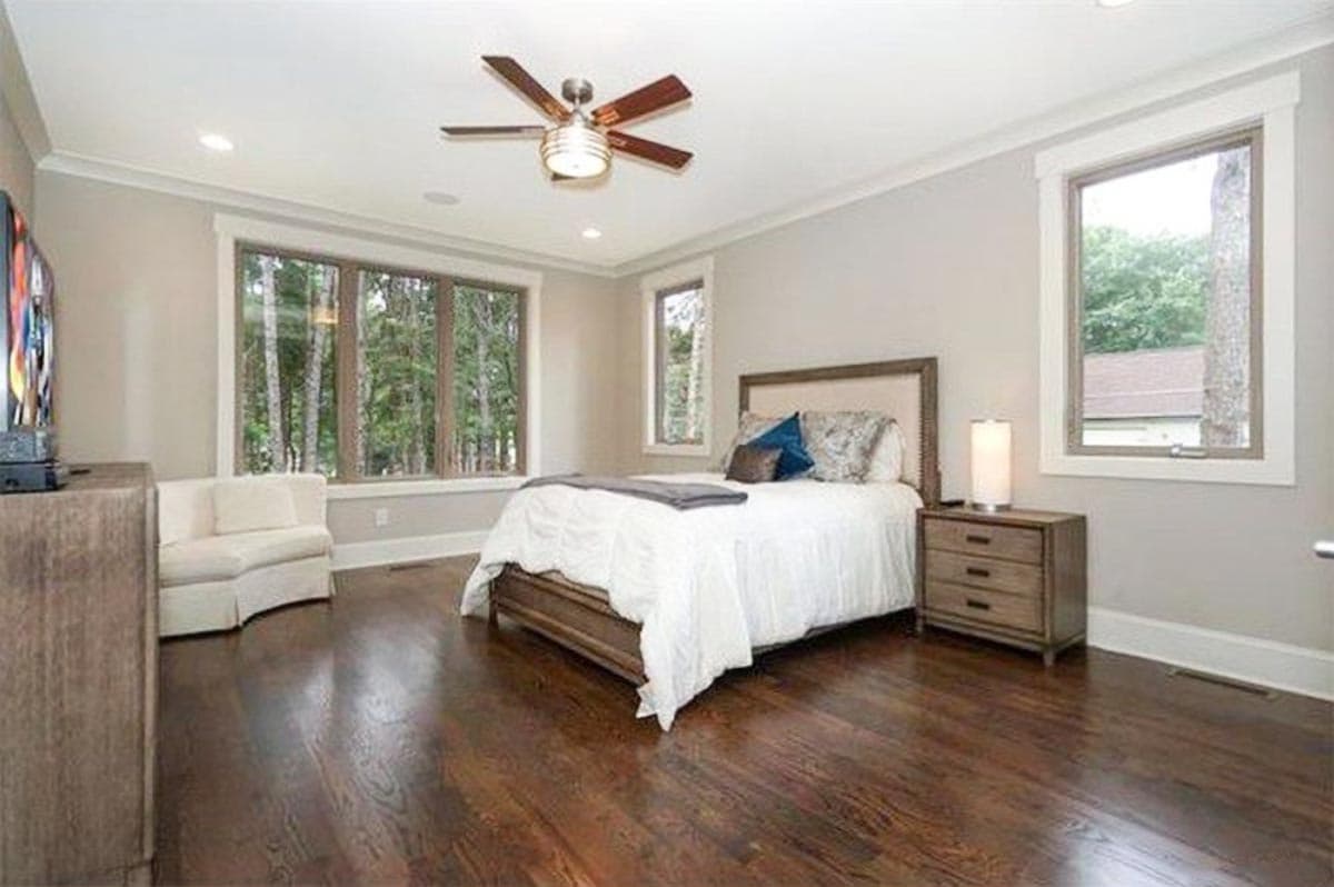 Interior rendering of a bedroom with a large window overlooking trees, a bed, and a ceiling fan.