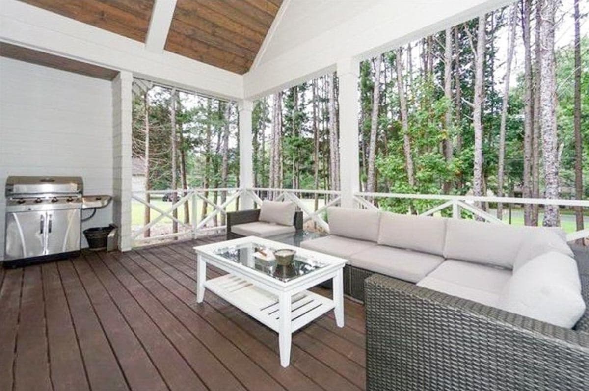 Covered porch with wood ceiling, seating area with grill, and view of wooded backyard.