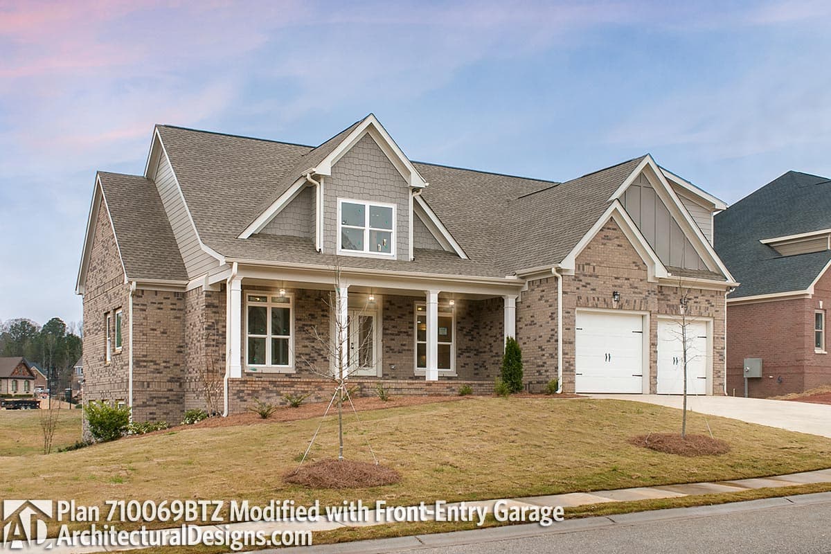 House plan exterior: One-story brick home with front-entry two-car garage, covered porch supported by columns, and dormer.