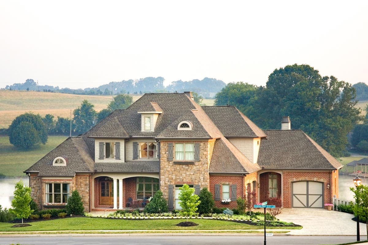 House plan exterior with stone and brick facade, multiple gables, arched entry, and dormer windows. Two-story with attached garage.