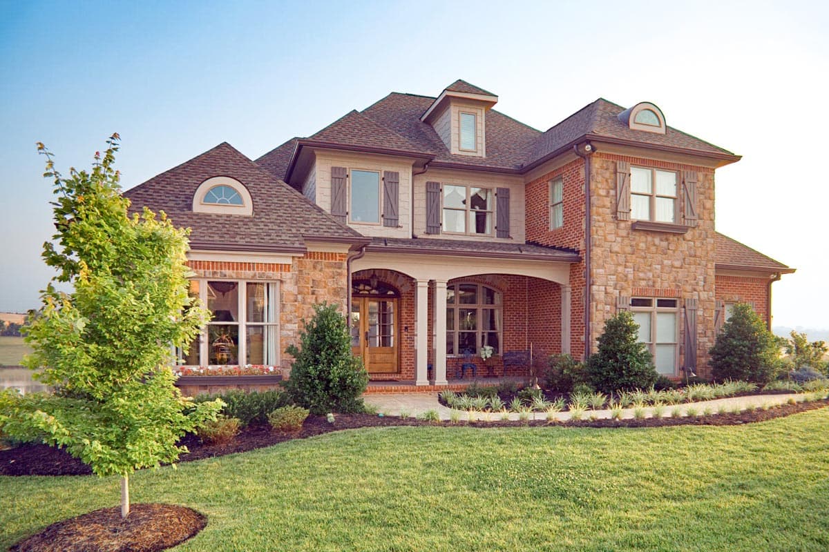 House plan exterior: Two-story home with stone and brick facade, arched entryway, dormer windows, and multi-gabled roof.