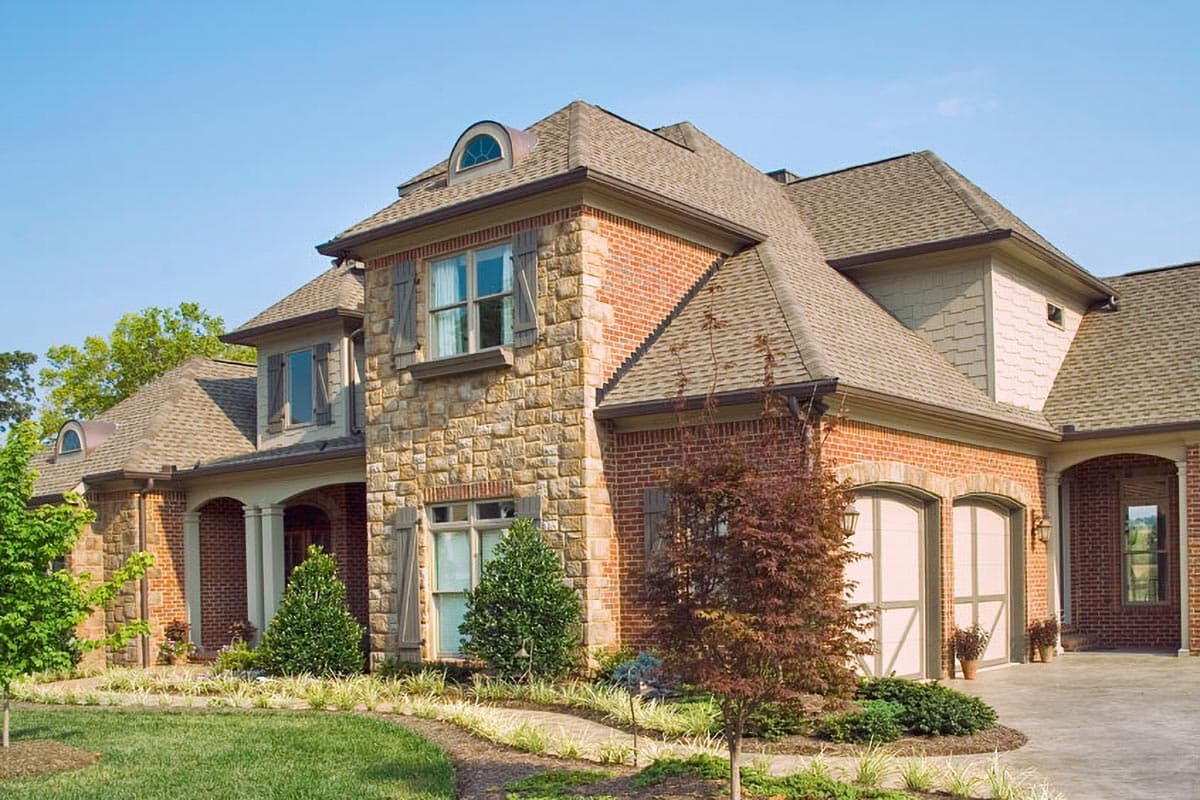 House plan exterior with stone and brick facade, dormer, and arched double garage doors.